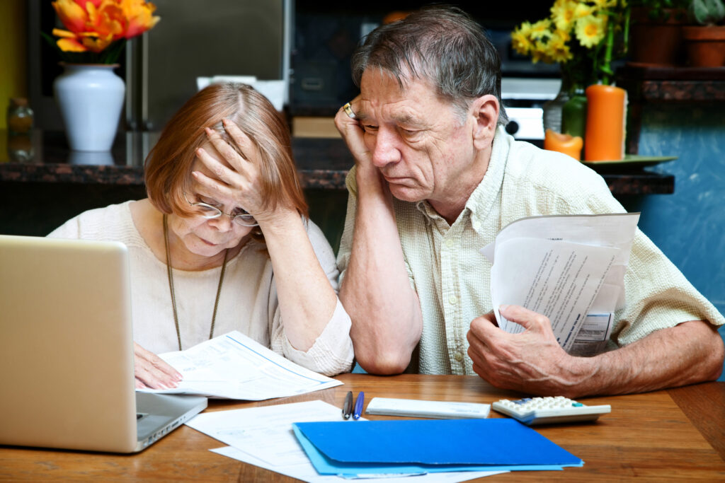 Senior couple looking worried while reviewing bills and financial documents at home, highlighting concerns about retirement finances in a volatile market.